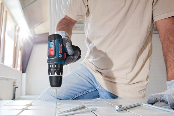 Eine Person bohrt mit einem Akkuschrauber ein Loch in eine weiße Fliese.